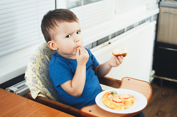 The little boy in the kitchen eating a small pizza