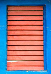 Fototapeta na wymiar Red wooden shutters closed on window on blue wall