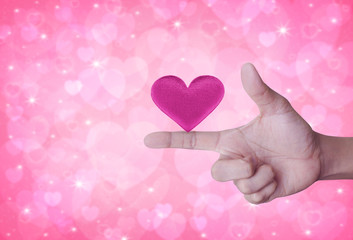Fabric pink love heart shape on finger over blur pink background, Valentines day concept