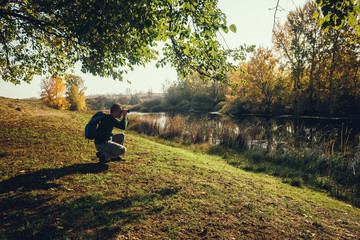 Man is watching birds with binoculars by the river in autumn.