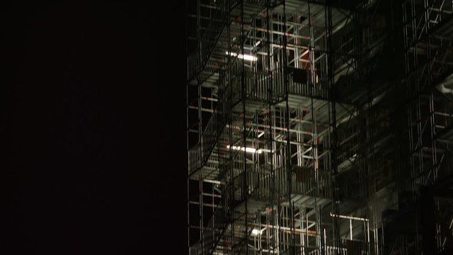 Camera tilts up a high series of scaffolding along a clock tower