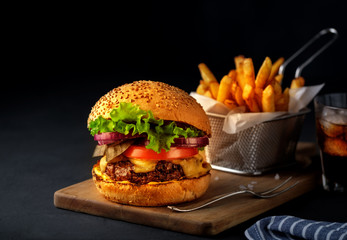 Tasty grilled beef burger with lettuce, cheese and onion served on cutting board on a black wooden...
