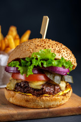 Tasty grilled beef burger with lettuce, cheese and onion served on cutting board on a black wooden table.