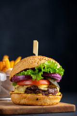 Tasty grilled beef burger with lettuce, cheese and onion served on cutting board on a black wooden table, with copyspace.