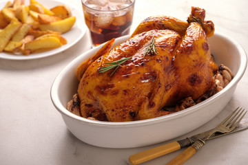 Roasted chicken with garlic in a white deep plate on a white table
