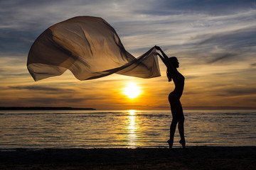 summer background - silhouette of slim sexy girl in bikini posing with scarf on the beach