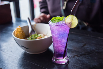 Butterfly pea iced soft drinks with lemon slice and peppermint on top and on the wooden table at the riverside restaurant.Thailand.