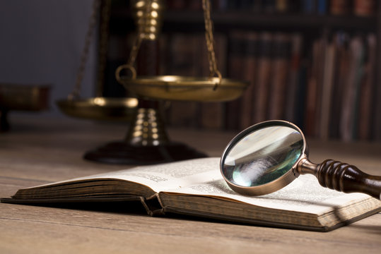 magnifying glass, scales of justice and law books in the background