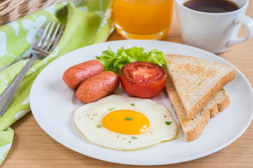 Breakfast with fried egg, toast, sausage, vegetable, coffee and orange juice on table