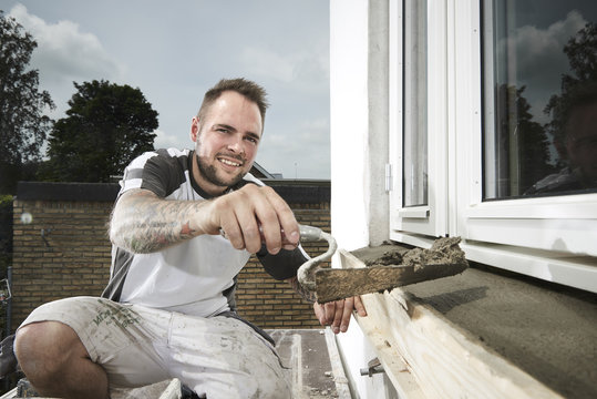 Bricklayer and his bricklayer&acute;s assistant working at a house