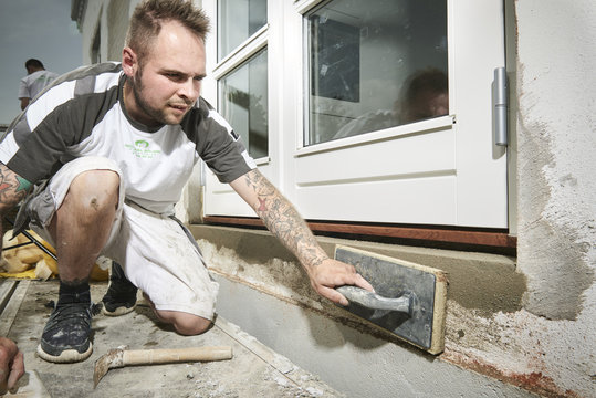 Bricklayer and his bricklayer&acute;s assistant working at a house