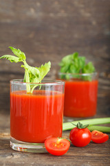 Glass of tomato juice with cherry tomatoes and celery leaves on wooden table, vertical