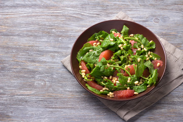 Fresh salad from arugula with grapefruit and pine nuts on a wooden background. Healthy delicious food