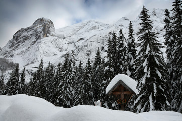 Wood tabernacle in front of innevated forest near Alba di Canazei, Val di Fassa. Trentino Alto-Adige, Italy.