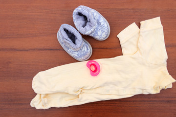 Baby clothes, booties and soother on wooden background