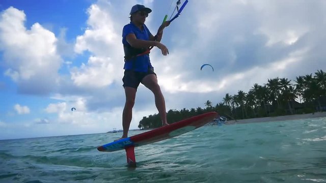 Wide angle shot of kitesurfer riding a foil flying over water in tropical island