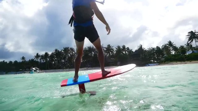 Wide angle shot of kitesurfer riding a foil flying over water in tropical island
