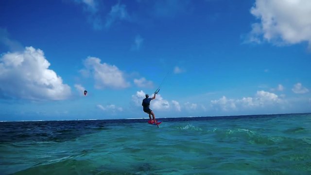 Wide angle shot of kitesurfer riding a foil flying over water in tropical island