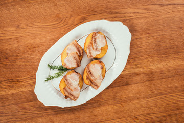 baked potatos with ham slices on top laying on plate over wooden surface
