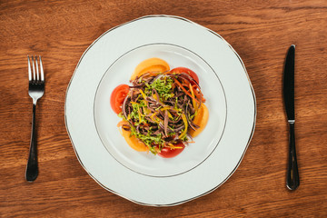 fresh vegetables surrounded by tomatos sliced on white plate over wooden surface  with fork and knife