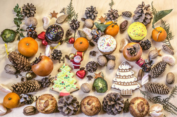 Christmas cookies,toy Santa Claus,fruits,nuts, pine cones with chocolate sweets on a plywood table