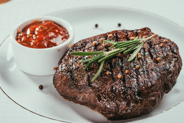 Close-up view of grilled steak with pepper, rosemary and sauce on white plate