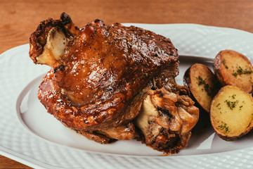 Close-up grilled meat on bone with potatoes on white plate