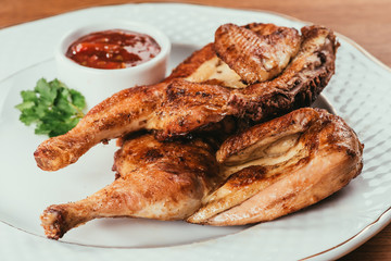 grilled chicken laying on plate with red sauce in saucer over wooden surface