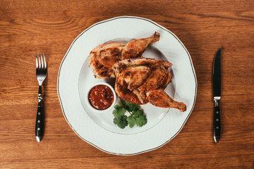 Top view of grilled chicken served on plate with sauce on wooden table
