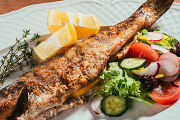 Baked fish with lemon and herbs on white plate with salad