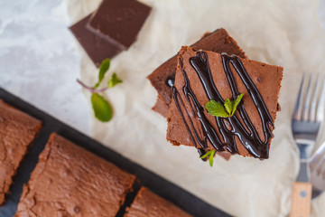 Pieces of healthy vegan pumpkin chocolate brownie with chocolate (carob) syrup on slate board, top view.