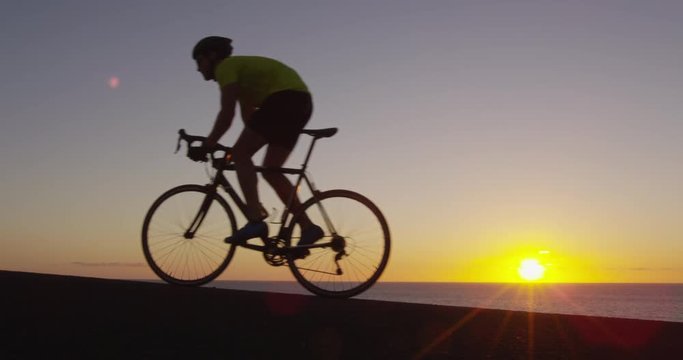 Road bike cyclist sports athlete biking cycling outdoors silhouette near ocean. Professional triathlete riding bike on an open road to the sunset. Active healthy man sport lifestyle. Shot on RED epic.