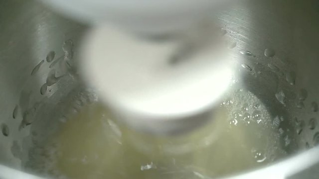 The mealted butter is being beaten with sugar and eggs by the electric whisk. The sweet mass is in the deep steel pot and the machine is fastly running and turing around. The future dough is foaming