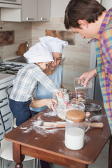 mother and son preparing dough for cookies while father pouring milk into bowl