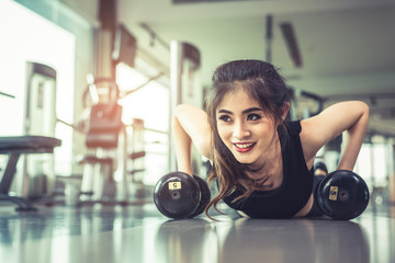 Fototapeta na wymiar Asian young woman doing push ups with dumbbell on floor in fitness gym and equipment background. Workout and Sport Exercise concept. Healthy and Happiness concept. Beauty and Body build up theme.