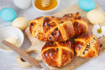 Easter cross buns on a wooden board, painted eggs. Light background, copy space, Easter food concept.