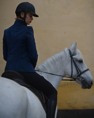 Look from behind at woman in blue riding white horse.
