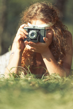 Pretty hippie girl on the grass taking photos with an old camera - Vintage effect photo