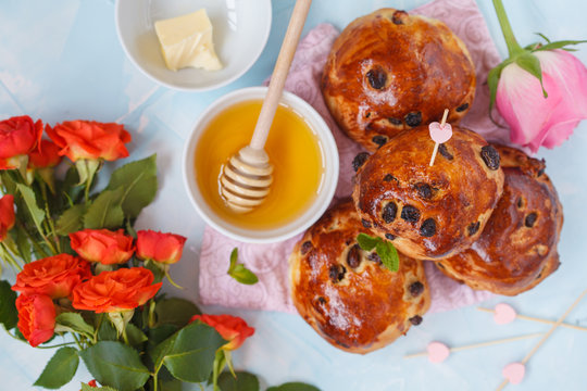 Breakfast for Valentine's Day. Buns with raisins, butter and honey, bouquet of flowers. Top view, blue background. Valentine's Day concept.