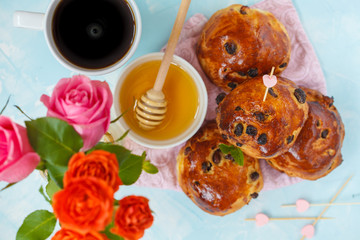 Breakfast for Valentine's Day. Buns with raisins, butter and honey, coffee, bouquet of flowers. Top view, blue background. Valentine's Day concept.