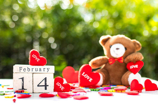 Wooden calendar show date of February 14 , valentine day , there are red hearts around , and teddy in background