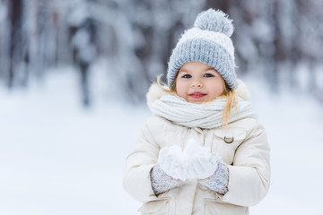 portrait of adorable kid holding snow ball in hands in winter park