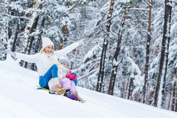 happy daughter and mother sledging together in winter park