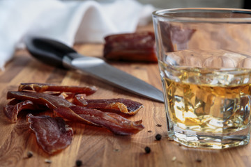 whiskey in a glass and sliced cured meats with spices on oak surface