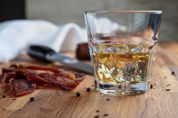 whiskey in a glass and sliced cured meats with spices on oak surface