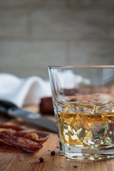 whiskey in a glass and sliced cured meats with spices on oak surface