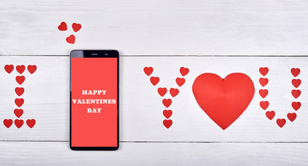 Close up of mobile smart phone with sign Happy Valentines day and red paper hearts on wooden background, copy space. Flat lay, top view. Valentines day application mockup. I love you