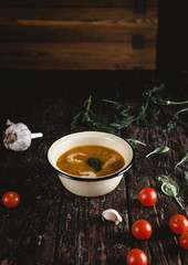 Soup with shrimps in bowl with tomatoes and herbs on wooden table