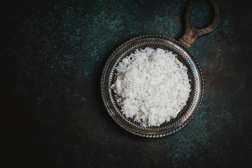 Top view of cooked white rice on rustic metal tray on dark table