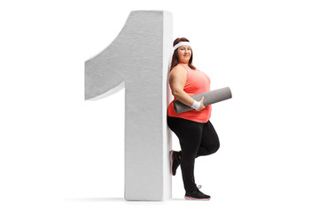 Overweight woman with an exercise mat leaning against a cardboard number one